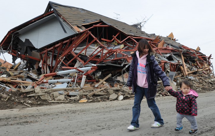 A child and her mother are seen walking past a damaged house in the earthquake and tsunami ravaged town of Natori, Migagi Prefecture, Japan, 14 March 2011. Tens of thousands of people were feared dead after last week's earthquake and tsunami in north-eastern Japan as Prime Minister Naoto Kan said 15,000 people had been rescued so far.  EPA/ALEX HOFFORD