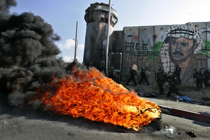 Israeli soldiers run past burning tires under a mural of the late Palestinian leader Yasser Arafat during clashes with Palestinian stone throwers following a protest to mark the upcoming 63rd anniversary of "Nakba", Arabic for "Catastrophe", the term used to mark the events leading to Israel's founding in 1948, in the Qalandia checkpoint between Ramallah and Jerusalem, Saturday, May 14, 2011.(AP Photo/Majdi Mohammed)