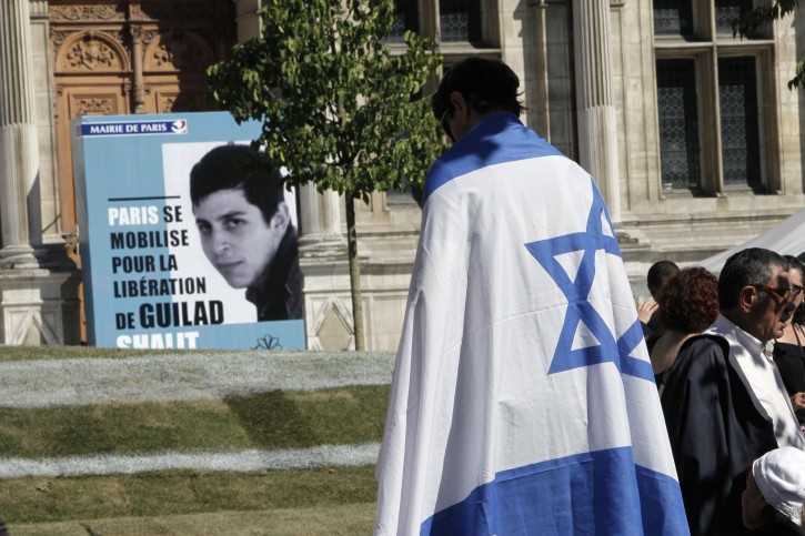 A man draped in an Israeli flag stands near to a poster depicting Israeli soldier Gilad Schalit displayed at the Paris Town hall, Sunday, June 26, 2011, to mark 5th anniversary of his snatching by Palestinian militants. Schalit has been held by Hamas since June 25, 2006, when he was captured in a cross-border raid. His captors have refused Red Cross visits and contact with his family and his condition is unknown. Placard reads 'Paris mobilizes for the liberation of Guilad Shalit'. (AP Photo/Thibault Camus)