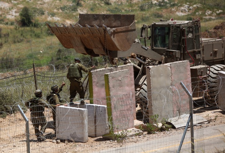  Israeli soldiers observe the scene as an army bulldozer adds some concrete parts to fortify the border line between the Israeli-controlled Golan Heights (foreground) and Syria (behind) beneath the so-called 'Shouting Hill,' at Majdal Shams, Israel, on 07 June 2011.  EPA/ATEF SAFADI