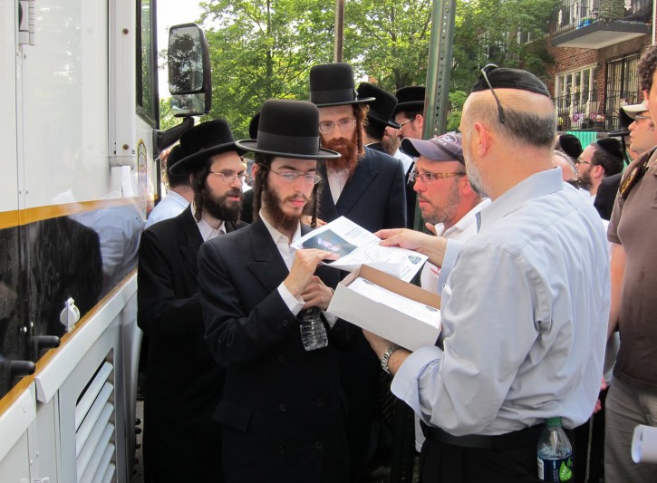 In this July 12, 2011, photo provided by VosIzNeias.com, volunteers gather at a Flatbush Shomrim Safety Patrol (FSSP) Mobile Command Center  in the Borough Park neighborhood of Brooklyn, New York, where they are given fliers to post after 8-year-old Leiby Kletzky was reported missing the previous day. When the  boy from the insulated, ultra-Orthodox Jewish neighborhood failed to make it home from day camp, his parents' first call was not to the police, but to the Shomrim patrol, a local volunteer group whose name means guardians in Hebrew. In the days before he was found dead, the search party to find Leiby grew to as many as 5,000 people. (AP Photo/VosIzNeias.com, Eli Wohl)