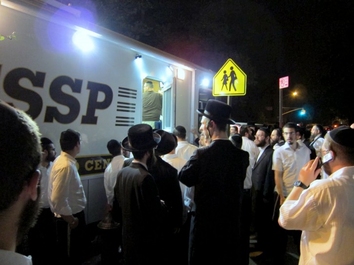 In this July 11, 2011 photo provided by VosIzNeias.com, volunteers gather around a Flatbush Shomrim Safety Patrol (FSSP) Mobile Command Center in the Borough Park neighborhood of Brooklyn, New York after 8-year-old Leiby Kletzky was reported missing earlier in the day. When the  boy from the insulated, ultra-Orthodox Jewish neighborhood failed to make it home from day camp, his parents' first call was not to the police, but to the Shomrim patrol, a local volunteer group whose name means guardians in Hebrew. In the days before he was found dead, the search party to find Leiby grew to as many as 5,000 people. (AP Photo/VosIzNeias.com, Eli Wohl)