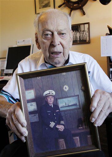 In this April 12, 2012 photo, an 88-year-old retired Coast Guard captain, who declined to be identified for fear of being targeted for fraud again, displays a photo of himself in uniform taken some four decades ago as he sits in his home in Bothell, Washington. A Jamaica-U.S. task force launched three years ago to stop a network of aggressive gangs who use fake lottery scams has failed to stop the con artists, who are now stealing an estimated $1 billion a year, largely from elderly Americans. (AP Photo/Elaine Thompson)