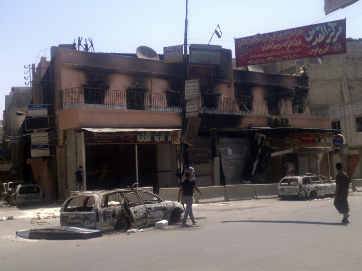 This citizen journalist image shows people walking past a gutted police station flying the Syrian revolutionary flag after fighting between rebels and Syrian troops in the Yarmouk camp for Palestinian refugees in south Damascus, Syria, Saturday, July 21, 2012. (AP Photo)