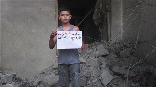 In this citizen journalism image provided by Shaam News Network SNN, taken on Wednesday, July 11, 2012, a Syrian boy holds a poster with Arabic that reads, "and what happens after press conferences, even more press conferences!" in Homs, Syria. (AP Photo/Shaam News Network, SNN)T