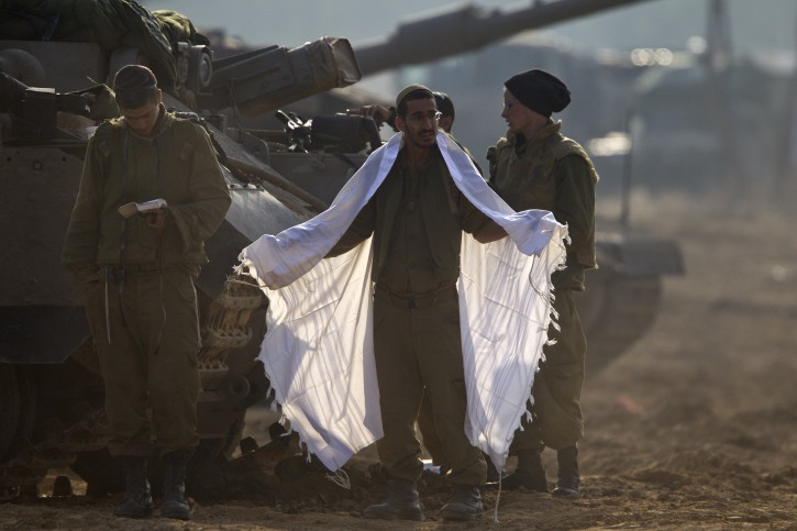  An Israeli soldier prepares for morning prayers at his APC (Armoured Personnel Carrier) on a tank staging area in southern Israel along the border with the Gaza Strip, 19 November 2012. Behind, a group of religious soldier take part in morning prayers. Reports state that the Israeli military is prepared to significantly widen operations against Palestinian militants in the Gaza Strip. EPA