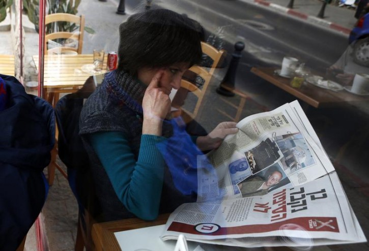 A woman is seen through a coffee shop window as she reads an article about Ben Zygier in an Yedioth Ahronoth newspaper in Jerusalem February 15, 2013. Zygier, the Australian immigrant reported to have been recruited by Israel's Mossad spy agency, was charged with grave crimes before he committed suicide in an Israeli jail, one of his lawyers said on Thursday. REUTERS/Baz Ratner (