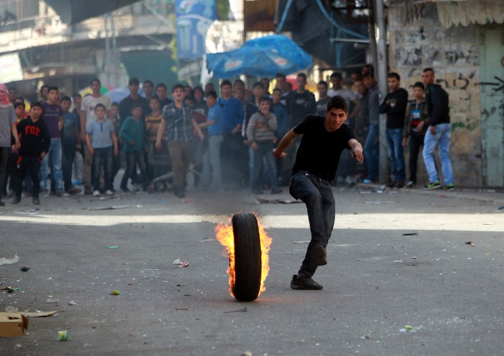 A Palestinian runs next to a burning car tire during clashes with Israeli riot police in Hebron, the West Bank, 14 March 2013. EPA/ABED AL HASHLAMOUN