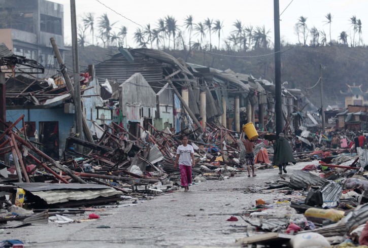 Residents walk past damaged structures in Tacloban city, Leyte province central Philippines on Sunday, Nov. 10, 2013. The city remains littered with debris from damaged homes as many complain of shortage of food, water and no electricity since the Typhoon Haiyan slammed into their province. Haiyan, one of the most powerful typhoons ever recorded, according to U.S. Navy's Joint Warning Center, slammed into central Philippine provinces Friday leaving a wide swath of destruction and scores of people dead.  (AP Photo/Aaron Favila)