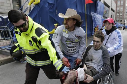 FILE - An emergency responder and volunteers, including Carlos Arredondo in the cowboy hat, push Jeff Bauman in a wheelchair after he was injured in an explosion near the finish line of the Boston Marathon Monday, April 15, 2013 in Boston. AP