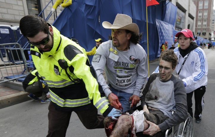 In this April 15, 2013 file photo, an emergency responder and volunteers, including Carlos Arredondo in the cowboy hat, push Jeff Bauman in a wheel chair after he was injured in an explosion near the finish line of the Boston Marathon Monday, April 15, 2013 in Boston. (AP Photo/Charles Krupa, File)