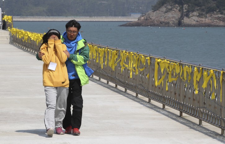 A woman relative of a passenger aboard the sunken ferry Sewol in the water off the southern coast is consoled by her husband  as yellow ribbons are displayed as a sign of hope for safe return of missing passengers at a port in Jindo, South Korea, Thursday, April 24, 2014. Divers made their way deeper Thursday into the submerged wreck of a ferry that sank more than a week ago as the death toll neared 160 and relatives of the more than 140 still missing pressed the government to finish the grim task of recovery soon.(AP Photo/Ahn Young-joon)