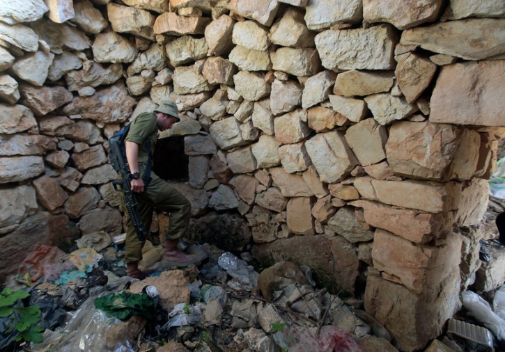 An Israeli soldier searching inside an unwed rural, Palestinian stone structure in the hills near the West Bank village of Halhoul, north of Hebron, for clues to the case of the missing three Israeli boys who were abducted and killed, on 29 June 2014. EPA/ABED AL HASHLAMOUN