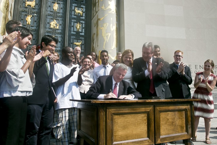 New York Mayor Bill de Blasio, center, receives applause he signs a law that paves the way for the city to create municipal identification cards, Thursday, July 10, 2014, outside the main Brooklyn library in New York. The cards, dubbed NYC ID, are expected to be available in January. They will be available to anyone who can prove their identity and residence in the nation's largest city.  In particular, they are expected to help the estimated 500,000 illegal immigrants who live in New York who would then able to provide an ID required to receive certain government services. (AP Photo/Bebeto Matthews)