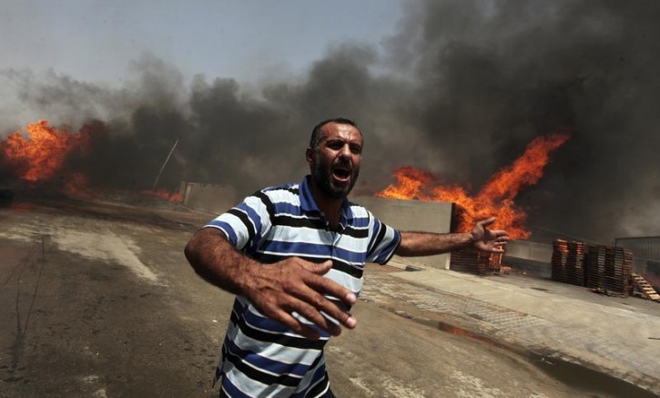 A Palestinian reacts in front of a fire which police said was caused by an Israeli tank shelling in the industrial area in the east of Gaza City July 12, 2014. I