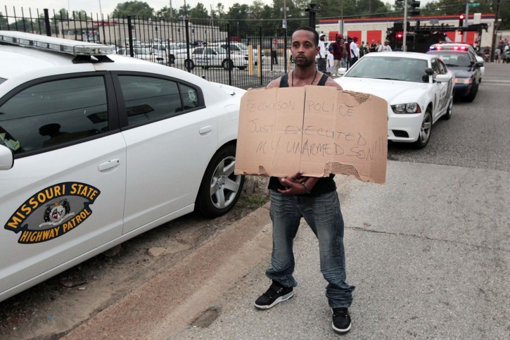 Louis Head, stepfather to 18-year-old Michael Brown who was fatally shot by police, holds a sign in Ferguson, Mo., near St. Louis on Saturday, Aug. 9, 2014. A spokesman with the St. Louis County Police Department, which is investigating the shooting at the request of the local department, confirmed a Ferguson police officer shot the man. The spokesman didn't give the reason for the shooting. (AP Photo/St. Louis Post-Dispatch, Huy Mach)