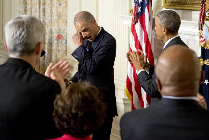President Barack Obama, right, and the audience applaud as Attorney General Eric Holder wipes his eye, in the State Dining Room of the White House in Washington, Thursday, Sept. 25, 2014, where the president announced that Holder is resigning. Holder, who served as the public face of the Obama administration's legal fight against terrorism and weighed in on issues of racial fairness, is resigning after six years on the job. He is the first black U.S. attorney general. (AP Photo/Carolyn Kaster)