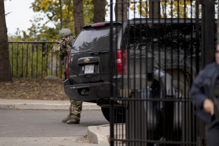 A heavily armed RCMP officer takes position at the gate of 24 Sussex Dr., the official residence of the Prime Minister, on Wednesday, Oct. 22, 2014.  A soldier standing guard at the National War Memorial has been shot by an unknown gunman and there have been reports of gunfire inside the halls of Parliament. (AP Photo/The Canadian Press, Justin Tang)