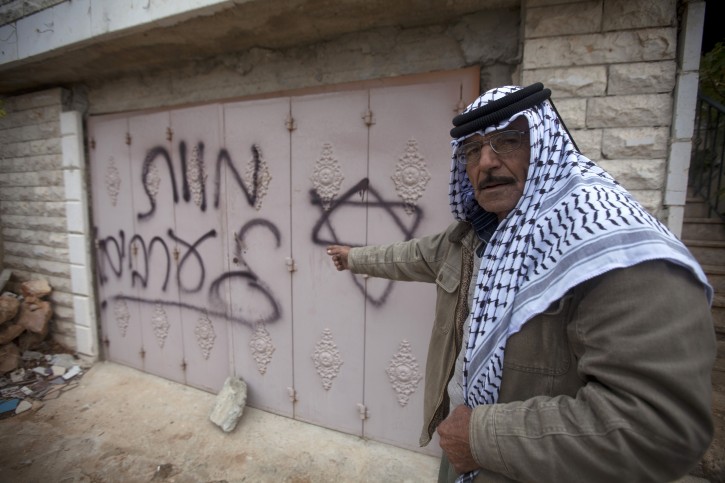 A Palestinian man points to Hebrew graffiti reading "Death to the Arabs" following an arson attack in Khirbet Abu Falah, northeast of the West Bank city of Ramallah, Sunday, Nov. 23, 2014. (AP Photo/Majdi Mohammed)