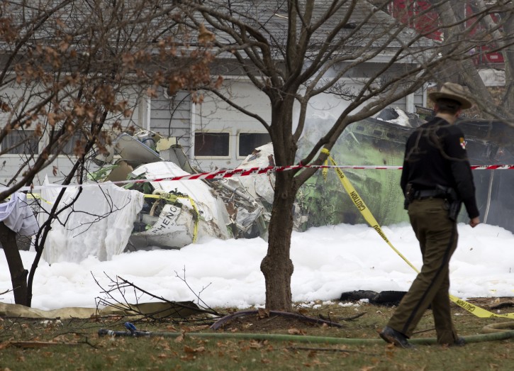 The wreckage of a small private jet smolders in a driveway after crashing into a neighboring house in Gaithersburg, Md., Monday, Dec. 8, 2014. A woman and her two young sons inside the home and three people aboard the aircraft were killed, authorities said. (AP Photo/Jose Luis Magana)