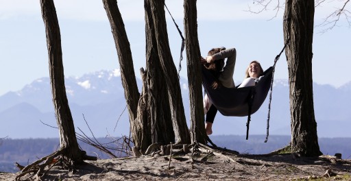 Taylor Wilkinson, right, and Karissa Courtney, both Seattle Pacific University students with the afternoon off, share a hammock overlooking the Puget Sound and the Olympic Mountains beyond Tuesday, Feb. 17, 2015, in Seattle. (AP Photo/Elaine Thompson)