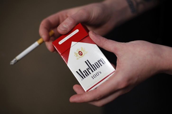 In this photo taken July 17, 2015, store manager Stephanie Hunt poses for photos with a pack of Marlboro cigarettes, an Altria brand, at a Smoker Friendly shop in Pittsburgh. Altria reports quarterly financial results on Wednesday, July 29, 2015. (AP Photo/Gene J. Puskar)