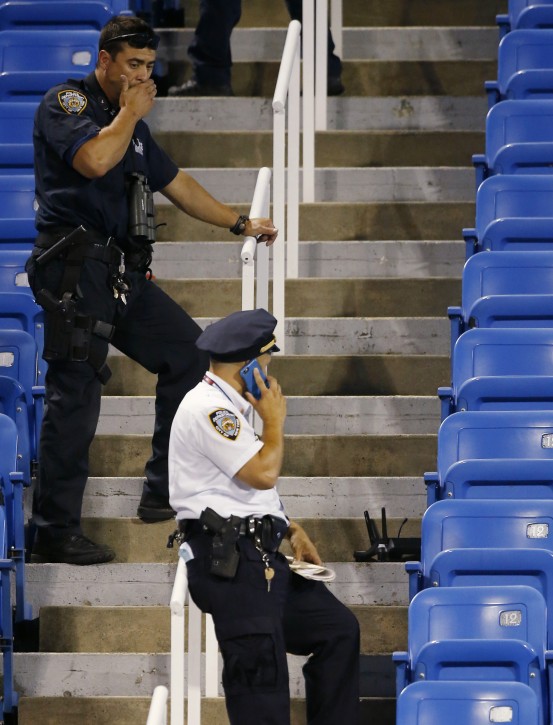 Police officers investigate the southwest corner of Louis Armstrong Stadium after a drone flew over the court, buzzing the players during a match between Flavia Pennetta, of Italy, and Monica Niculescu, of Romania, during the second round of the U.S. Open tennis tournament in New York, Thursday, Sept. 3, 2015.  The drone crashed into the seats and can be seen to the right of the police officer on his phone. (AP Photo/Kathy Willens)