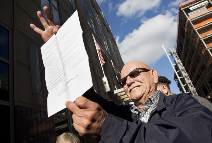Amaury Villalobos holds up the document showing that his conviction on arson and murder charges was overturned, Wednesday, Dec. 16, 2015, in New York. Villalobos and two other defendants were convicted of arson and six murders after a 1981 trial. Brooklyn District Attorney Ken Thompson asked the judge to clear the men. He says they were convicted based on outdated fire science and a lying witness. (AP Photo/Mark Lennihan)