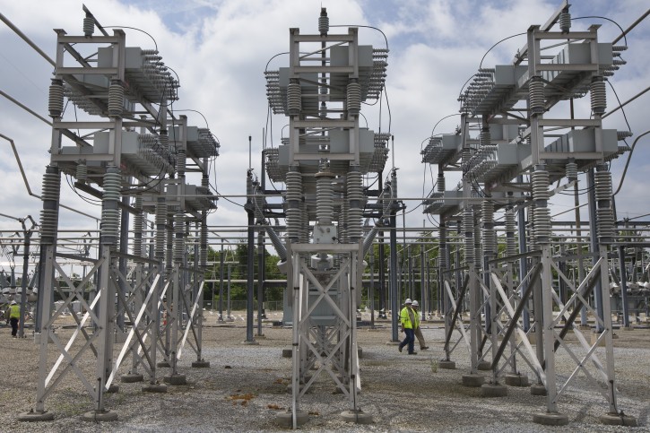 In this Wednesday, May 20, 2015 photo, contractors walk past a capacitor bank at an AEP electrical transmission substation in Westerville, Ohio. (AP Photo/John Minchillo)