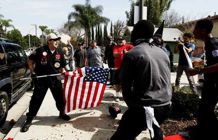 A Ku Klux Klansman, left, uses an American flag to fend off angry counter protesters after members of the KKK tried to start a "White Lives Matter" rally at Pearson Park in Anaheim, Calif., on Saturday, Feb. 27, 2016. The event quickly escalated into violence and at least two people had to be treated at the scene for stab wounds. (Luis Sinco/Los Angeles Times via AP)