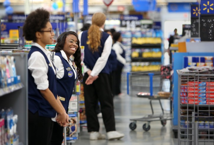 FILE- In this Wednesday, Jan. 27, 2016, file photo, Wal-Mart cashier Sandra Brown, second left, greets customers at the store in Horn Lake, Miss., after officially opening earlier in the day. Wal-Mart is bringing back greeters to a majority of its 5,000 U.S. stores. (Stan Carroll/The Commercial Appeal via AP, File)