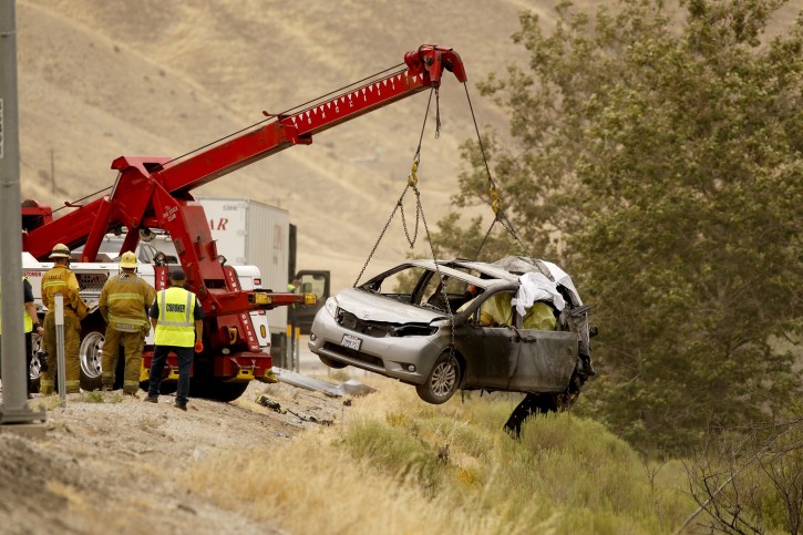 A heavy tow truck lifts a vehicle to the side of the 5 freeway as investigators look over the scene of an accident on Tuesday, June 28, 2016 in Gorman, Calif.  A minivan got in a minor collision and stopped on the shoulder. It was still partially in a lane when a semitrailer hit it and it burst into flames with two women and children inside, California Highway Patrol Officer Monica Posada said.  (Al Seib/Los Angeles Times via AP) 