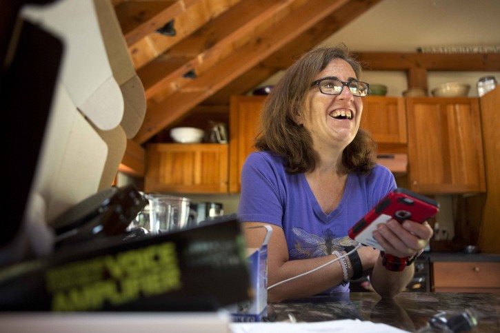 In this Friday, June 24, 2016, photo, Jessie Levine smiles as she listens to her recorded outgoing phone message on her iPhone in Springfield, N.H. Levine was diagnosed with Lou Gehrig's disease or ALS in 2015, and it has caused her speech to become slow and slurred. She is now exploring a new way to restore her voice via speech synthesis, or the artificial production of human speech. (AP Photo/Jim Cole)