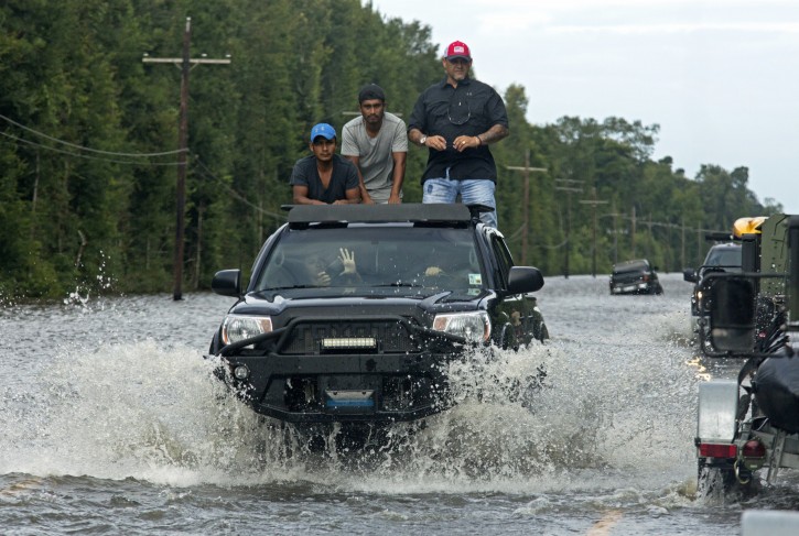 Motorists on Highway 190 drive through deep water through Holden, La., after heavy rains inundated the region, Sunday, Aug. 14, 2016. Louisiana Gov. John Bel Edwards said Sunday that at least 7,000 people have been rescued so far. (AP Photo/Max Becherer)