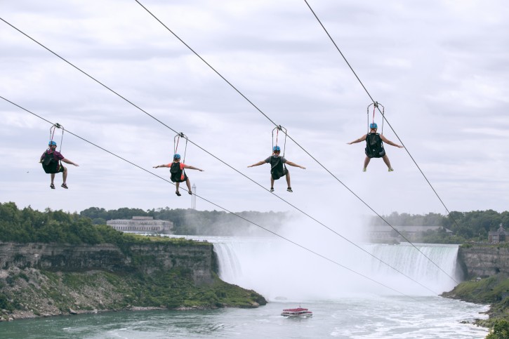 In this July 19, 2016 photo provided by WildPlay Ltd., tourists suspended above the water from zip lines make their way at speeds of up to 40 mph toward the the mist of the Horseshoe Falls, on the Ontario side of  Niagara Falls. The overhead cables have evolved from a fun way to explore jungle canopies to trendy additions for long-established outdoor attractions. (WildPlay Ltd./Kien Tran via AP)