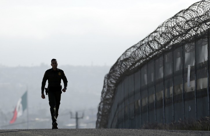 FILE - In this June 22, 2016, file photo, Border Patrol agent Eduardo Olmos walks near the secondary fence separating Tijuana, Mexico, background, and San Diego in San Diego. (AP Photo/Gregory Bull, File)