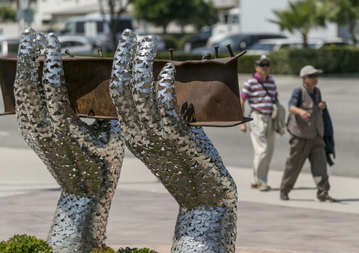 In this Friday, Aug. 26, 2016 photo, pedestrians walk by artist Heath Satow's sculpture "Reflect," made of two giant hands holding a a damaged, rusted I-beam from the collapsed World Trade Center buildings, outside the Rosemead City Hall plaza in Rosemead, Calif. The stainless steel 9/11 memorial sculpture is composed of 2,976 individual stylized dove silhouette representing a victim lost in the 9/11 terrorist attack on the U.S. in 2001. (AP Photo/Damian Dovarganes)