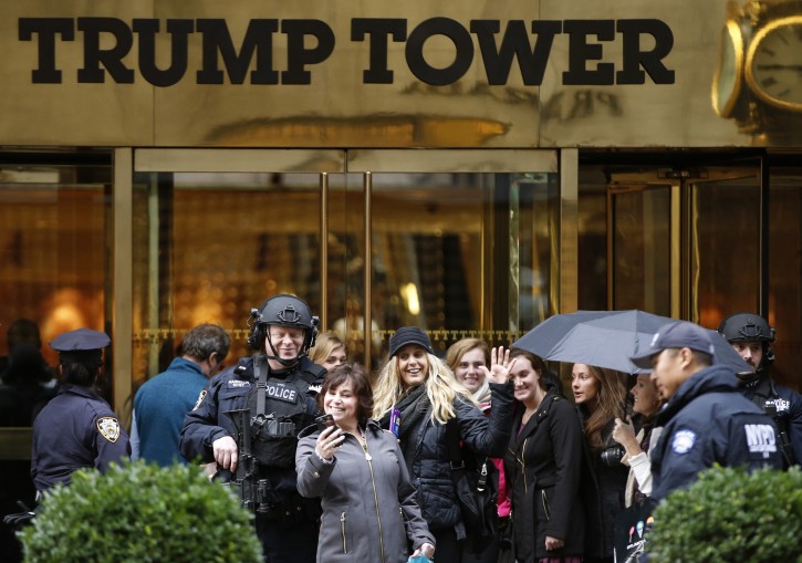 FILE- In this Nov. 15, 2016 file photo, a passersby stops for a selfie with a heavily-armed New York City police officer at the main, Fifth Avenue entrance to Trump Tower in New York. Outside Donald Trumpâs gilded skyscraper, many in the slow-moving sidewalk throng come for the sole purpose of snapping selfies, some to capture a bit of history and others to offer the new president their one-fingered salute. (AP Photo/Kathy Willens, File)
