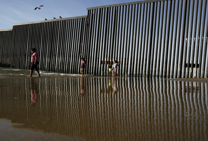 FILE - This Feb. 1, 2017 file photo shows the border structure separating San Diego from Tijuana, Mexico, reflected in the Pacific Ocean as people walk along the beach in Tijuana. The Trump administration has proposed spending $18 billion over 10 years to significantly extend the border wall with Mexico. The plan provides one of the most detailed blueprints of how the president hopes to carry out a signature campaign pledge. (AP Photo/Gregory Bull, File)
