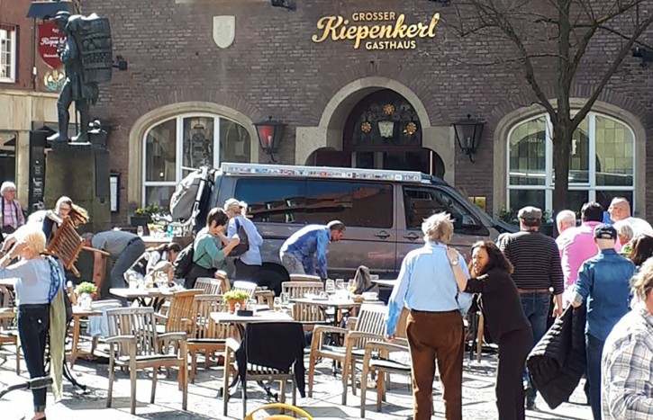 People stay in front of a restaurant in Muenster, Germany, Saturday, April 7, 2018 after a vehicle crashed into a crowd killing four people and injuring 20 others. The German news agency dpa has quoted police as saying the driver of that car in Muenster has killed himself. (Stephan R./dpa via AP)