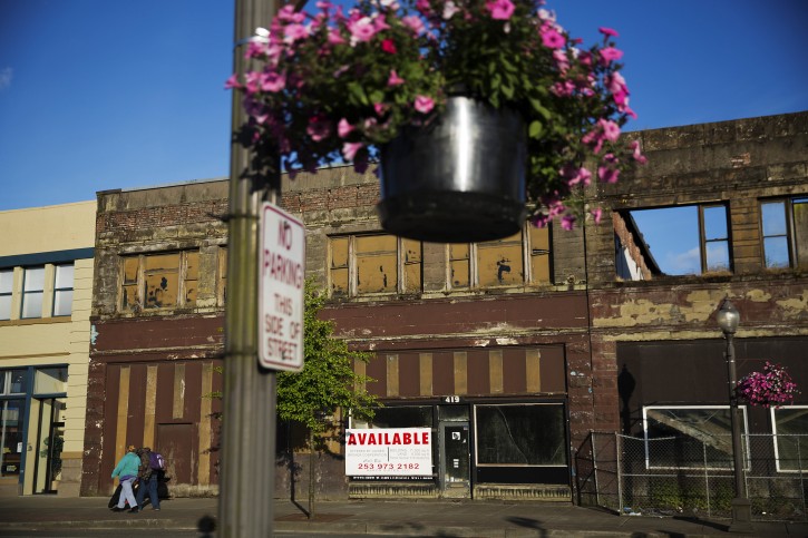 FILE- In this June 16, 2017, file photo, dilapidated storefronts stand along baskets of pink petunias that hang from light posts all over town, watered regularly by residents trying to make their city feel alive again in Aberdeen, Wash. AP