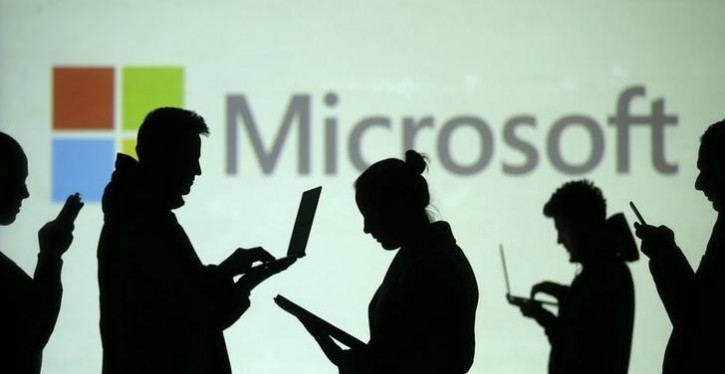 Silhouettes of laptop and mobile device users are seen next to a screen projection of Microsoft logo in this picture illustration taken March 28, 2018.  REUTERS/Dado Ruvic/Illustration