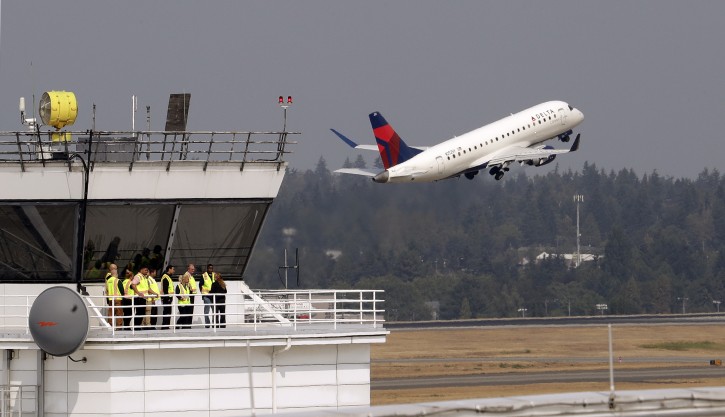People stand at the ramp tower, used to control airplane traffic into and out of 85 gates and 20 cargo hard stands, as a plane takes-off behind them at Seattle-Tacoma International Airport Monday, Aug. 13, 2018, in SeaTac, Wash. A turboprop plane was stolen from the airport by an airline ground agent on Friday, and later crashed into a small island in the Puget Sound, killing the man. (AP Photo/Elaine Thompson)