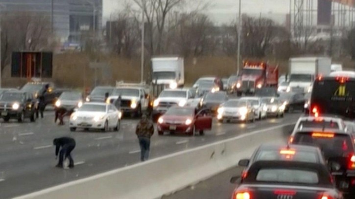 This screen shot from a video provided by Danielle Shah shows people picking up cash that spilled from an armored truck onto the highway in East Rutherford, N.J., near MetLife Stadium, Thursday, Dec. 13, 2018. Police say the incident caused multiple crashes as motorists stopped to grab the money from the truck that authorities say apparently had an issue with the locking device on one of its doors. (Danielle Shah/@dbholden417 via AP)