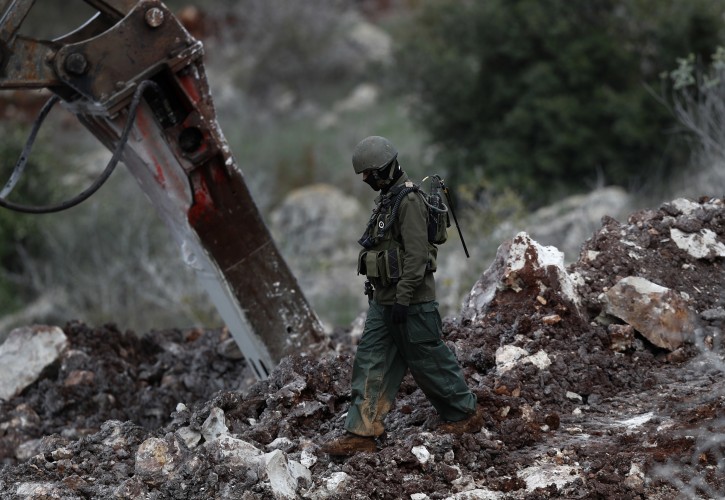 An Israeli soldier walks next to an excavator, near the southern border village of Mays al-Jabal, Lebanon, Thursday, Dec. 13, 2018. As Israeli excavators dig into the rocky ground, Lebanese across the frontier gather curiously to watch in real time what Israel calls the Northern Shield operation aimed at destroying attack tunnels built by Hezbollah.(AP Photo/Hussein Malla)