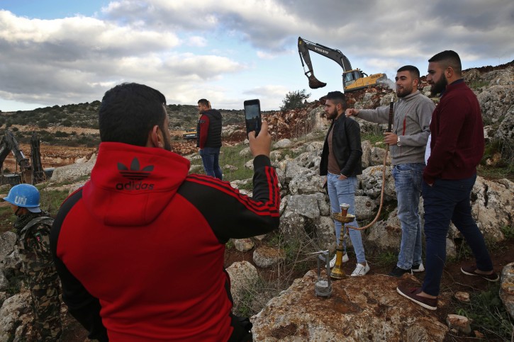 Lebanese villagers smoke water pipe and take souvenir pictures in front of Israeli excavators, in the Lebanese southern border village of Mays al-Jabal, Lebanon, Thursday, Dec. 13, 2018. As Israeli excavators dig into the rocky ground, Lebanese across the frontier gather curiously to watch in real time what Israel calls the Northern Shield operation aimed at destroying attack tunnels built by Hezbollah. (AP Photo/Hussein Malla)