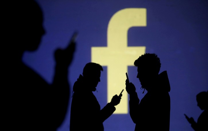 Silhouettes of mobile users are seen next to a screen projection of Facebook logo in this picture illustration taken March 28, 2018. REUTERS/Dado Ruvic