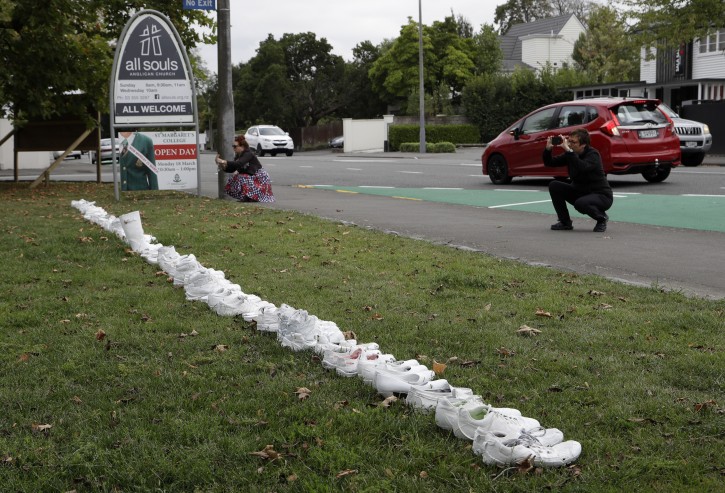 People photograph a memorial of 50 pairs of whites shoes for the victims of Friday March 15 mass mosque shootings in front of a church in Christchurch, New Zealand, Tuesday, March 19, 2019.  Four days after Friday's attack, New Zealand's deadliest shooting in modern history, relatives were anxiously waiting for word on when they can bury their loved ones. (AP Photo/Mark Baker)