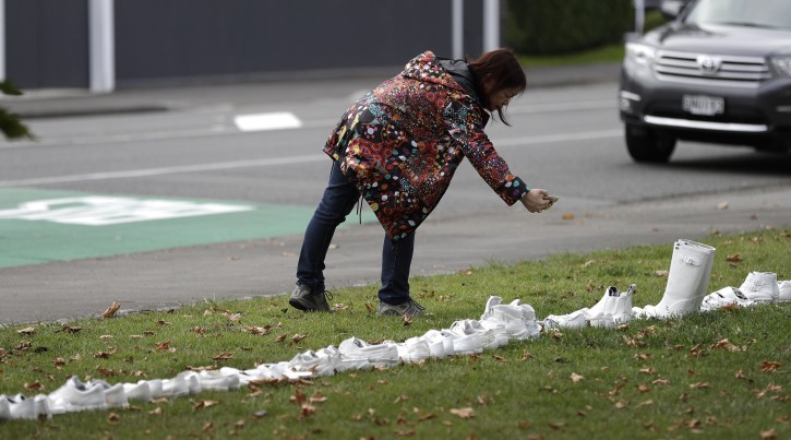 A woman photographs a memorial of 50 pairs of white shoes for the victims of Friday March 15 mass mosque shootings in front of a church in Christchurch, New Zealand, Tuesday, March 19, 2019.  Four days after Friday's attack, New Zealand's deadliest shooting in modern history, relatives were anxiously waiting for word on when they can bury their loved ones. (AP Photo/Mark Baker)