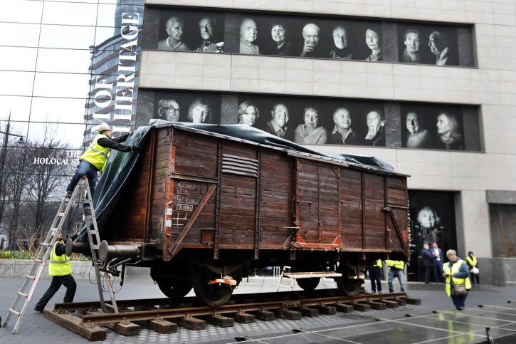 Portraits of Holocaust survivors are displayed at the Museum of Jewish Heritage as a vintage German train car, like those used to transport people to Auschwitz and other death camps, is uncovered on tracks outside the museum, in New York, Sunday, March 31, 2019.  (AP Photo/Richard Drew)